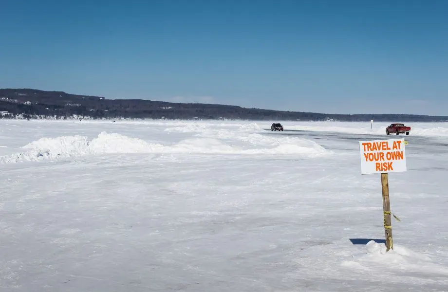Getting to Madeline Island in winter, cars driving along the frozen ice road with sign reading 'travel at your own risk'
