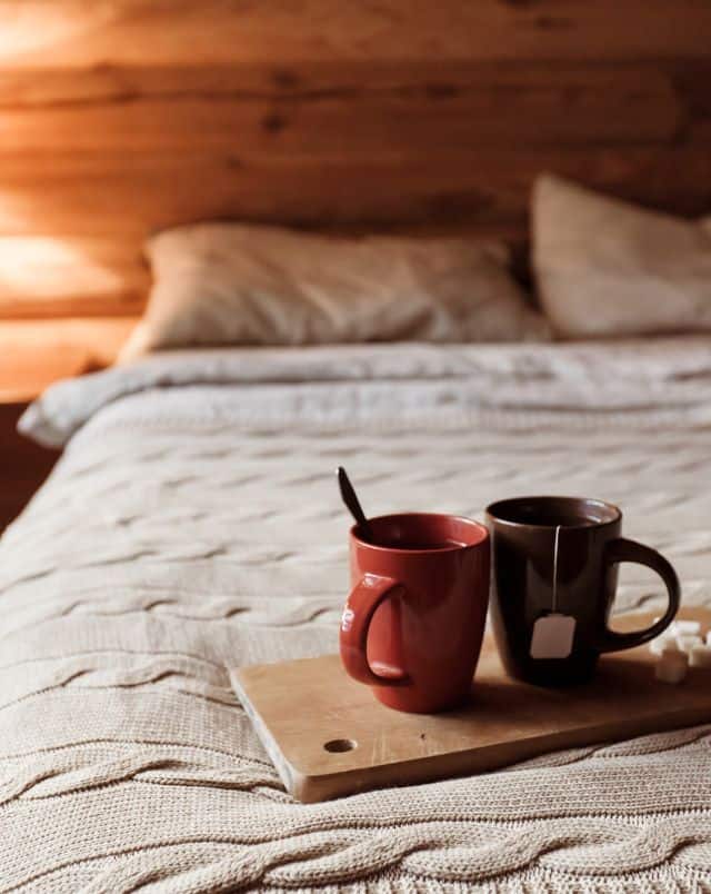 Best places for couples to go winter camping in Wisconsin, two mugs of tea on a wooden board with sugar cubes on top of a bed inside a cabin