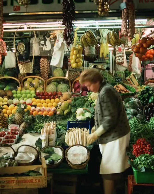  woman walking past a fruit and vegetable market stall in spain in november