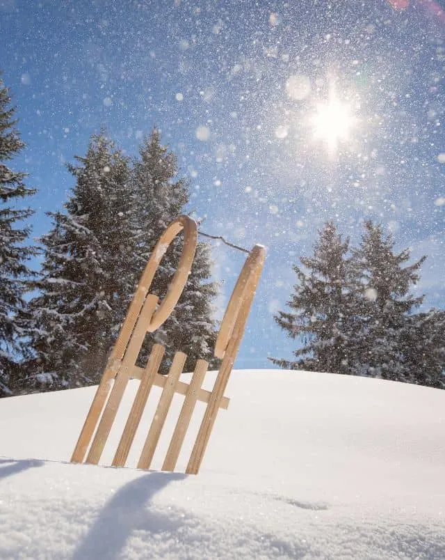 fun Door County February activities, wooden slay sticking up in snow bank with snow covered trees in background and flurries in the air on a bright sunny day