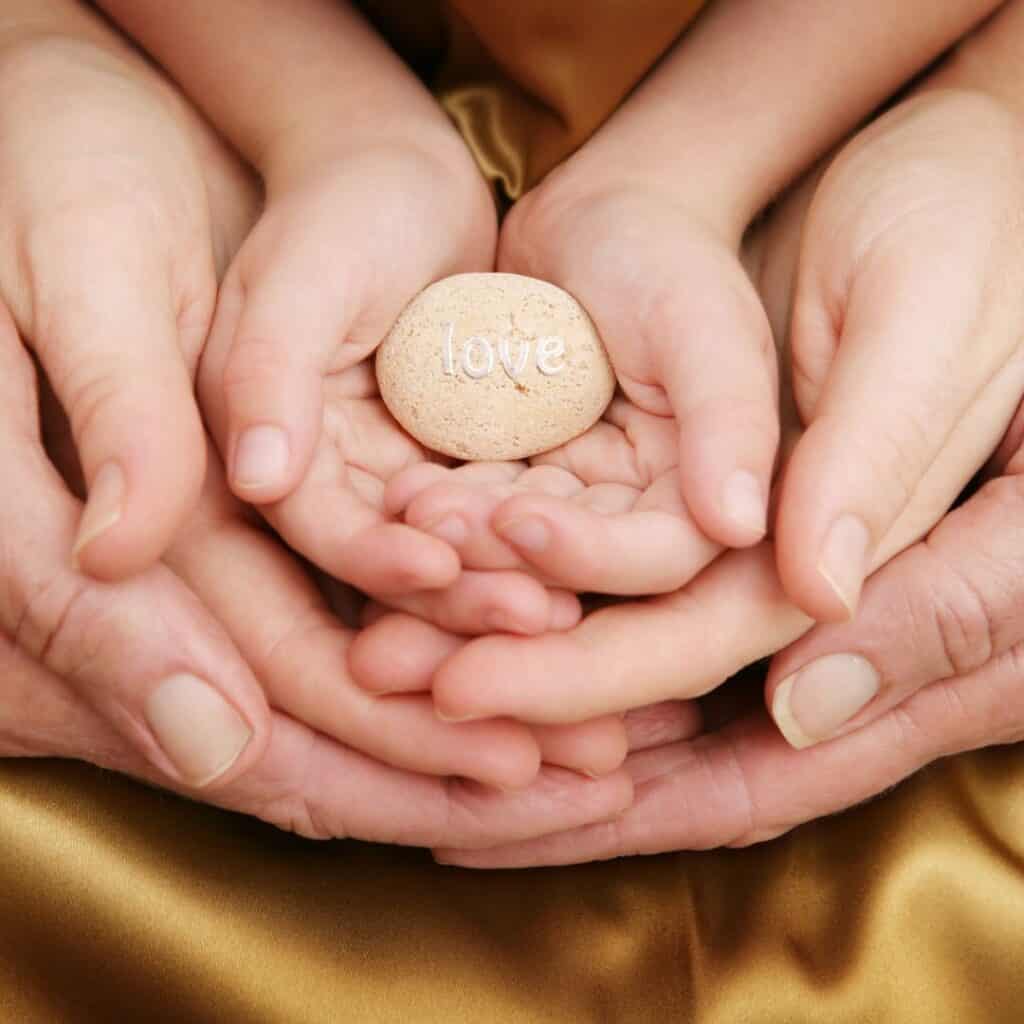 three pair of hands of a dad, mom, and child cradling a stone with 'love'