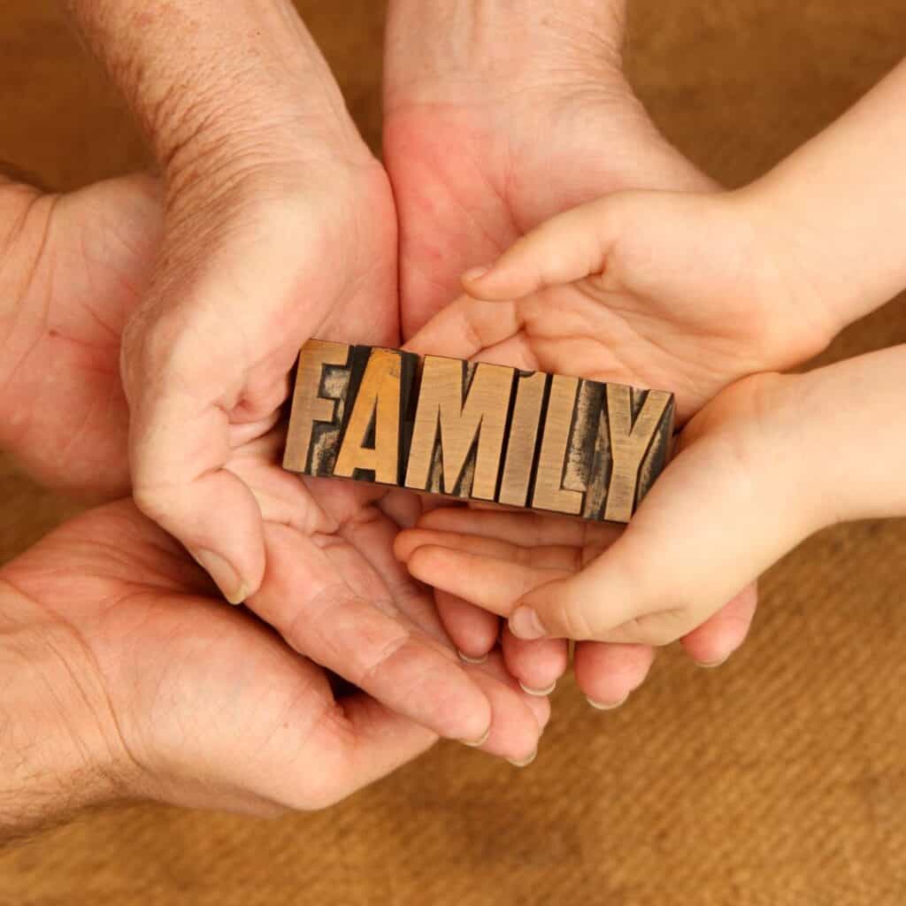 three pair of hands of a dad, mom, and child cradling the word family