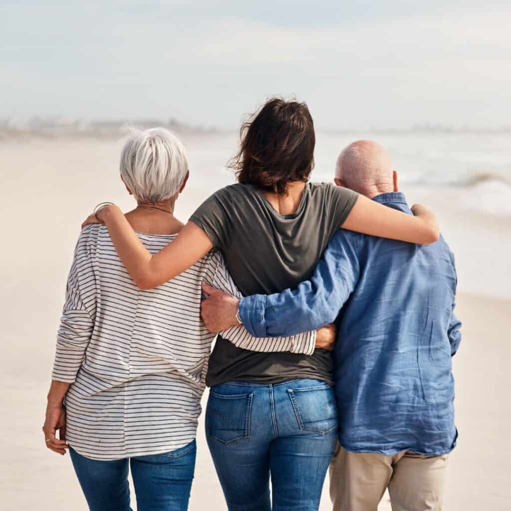 a daughter with her hands on her elderly parents shoulders walking together at the beach