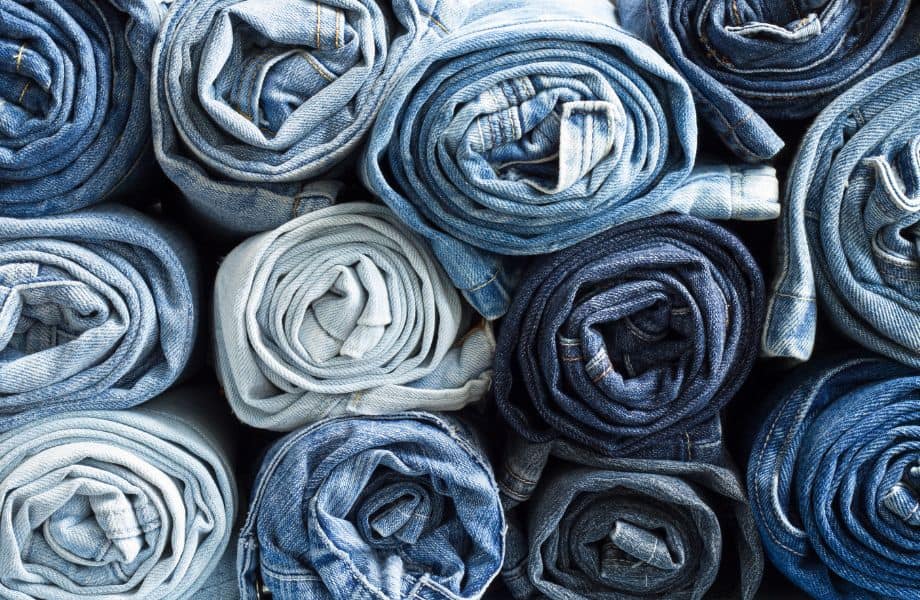 Best brands for sustainable jeans, stacks of rolled up jeans in different shades of blue
