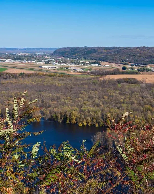 best Wisconsin road trips for families, aeriel view over rural Prairie du Chien with lake and trees in foreground and sparesly populated city in background next to a tree covered hill under a bright blue sky