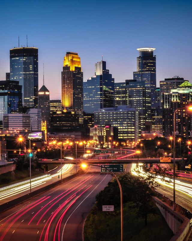 best road trips starting in Wisconsin, highway lined with red lights leading into downtown Minneapolis which is lit up at night