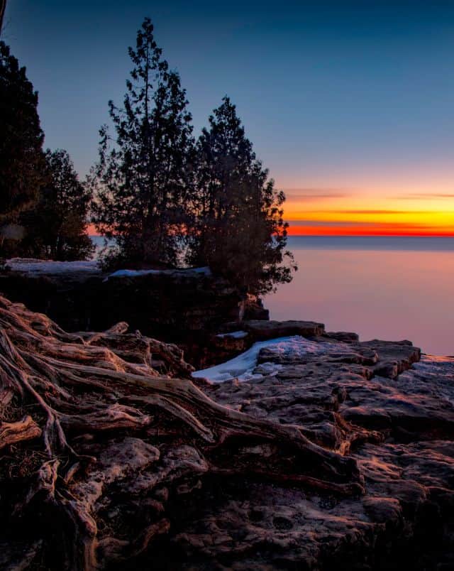 where to go for a Door County road trip, coastal area with trees and rocks at low sunset