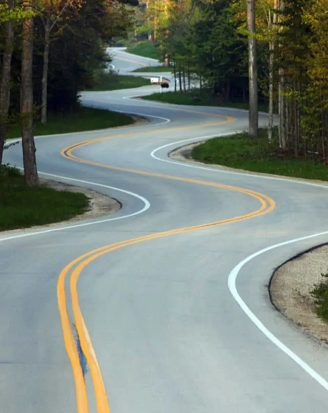 enjoy the best road trips in Wisconsin, empty winding road lined with trees and grass