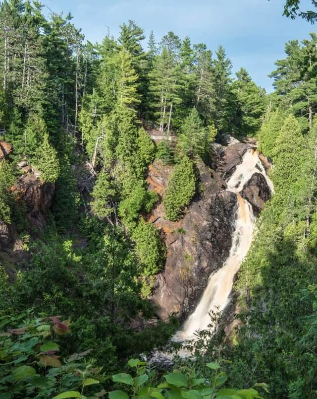 Northern Wisconsin road trips, tall waterfall surrounded by cliff and trees under a blue sky