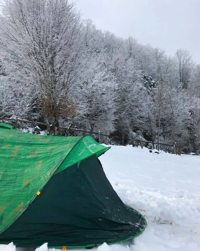 winter camping with kids in Wisconsin, green tent in snowy bank with snow covered trees in backgorund