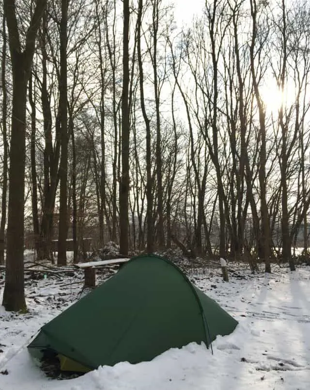 best year round campgrounds in Wisconsin, green tent in snowy campsite surrounded by trees with sun peeking through empty branches