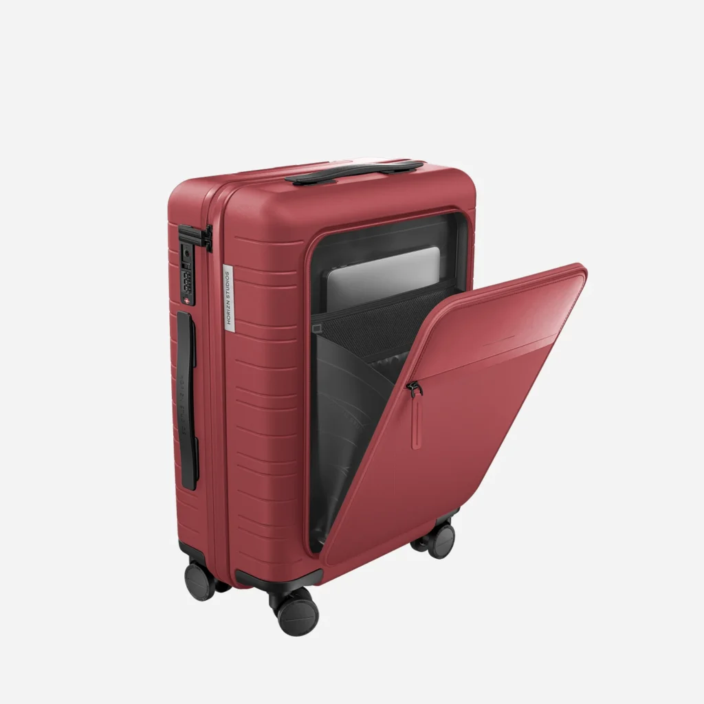 top eco-friendly luggage brands, metallic red wheelie suitcase with front pouch unzipped to show laptop inside