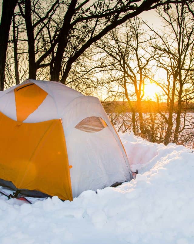 where to find Wisconsin winter camping, orange and white tent next to leaf-less tree and surrounded by snow with lake and sunrise in background