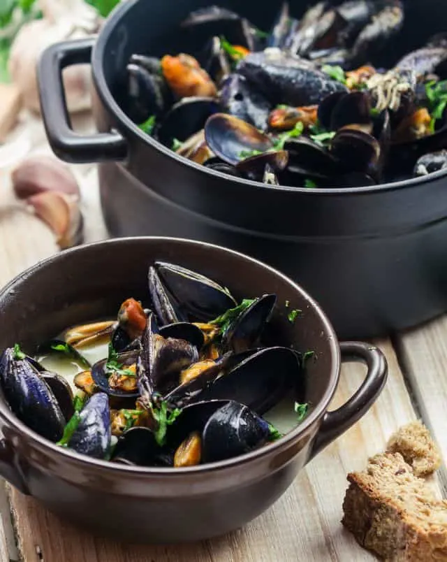 where to get the best authentic belgian food, bowl of mussels in broth next to large black pot of mussels