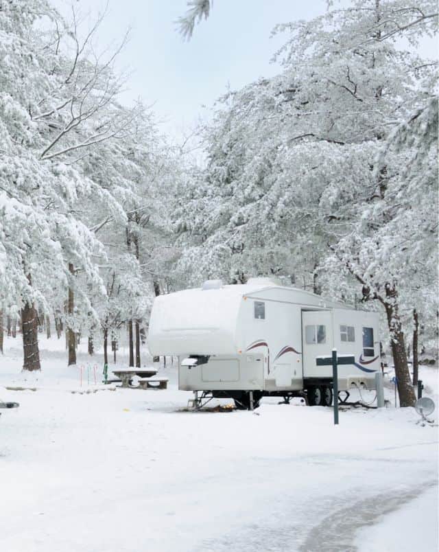 winter rv camping in Wisconsin, RV camper parked at campsite with table surrounded by snow and snow covered trees