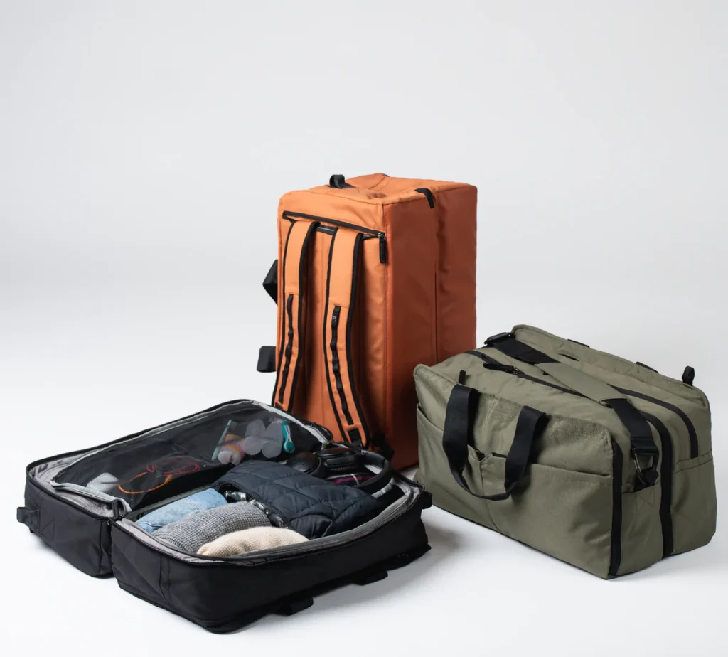 best brands for sustainable travel bags, three large duffel bags, an orange one showing backpack straps, an olive green one showing a duffel strap and an open black one displaying packed contents for travel
