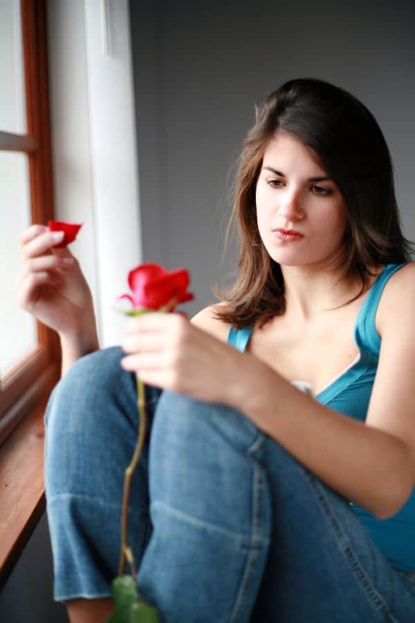 sad girl doing he loves me or he loves me not on roses petals