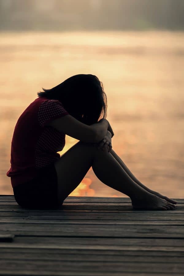 girl hunched feeling sad with sunset on the background