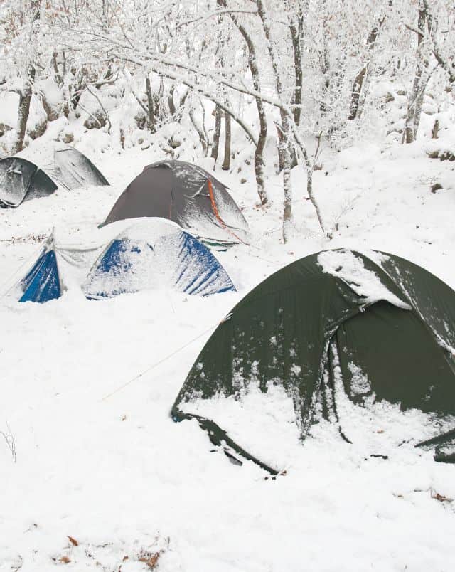 top winter campgrounds in Wisconsin, four snow-covered tents next to snow covered trees and ground