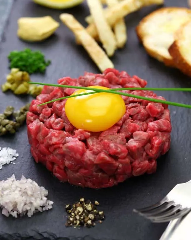 where to go for delicious classic belgian food, plate with steak tartare surrounded by piles of spices, french fries and bread slices