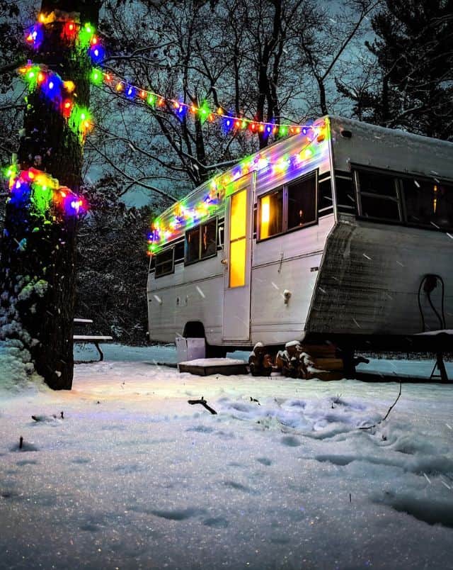 best winter camping Wisconsin offers, RV camper parked in snowy campsite with fairy lights hooked up to camper and nearby tree