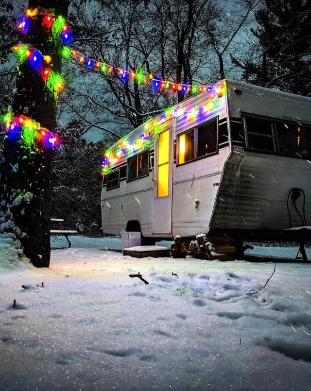 best winter camping Wisconsin offers, RV camper parked in snowy campsite with fairy lights hooked up to camper and nearby tree