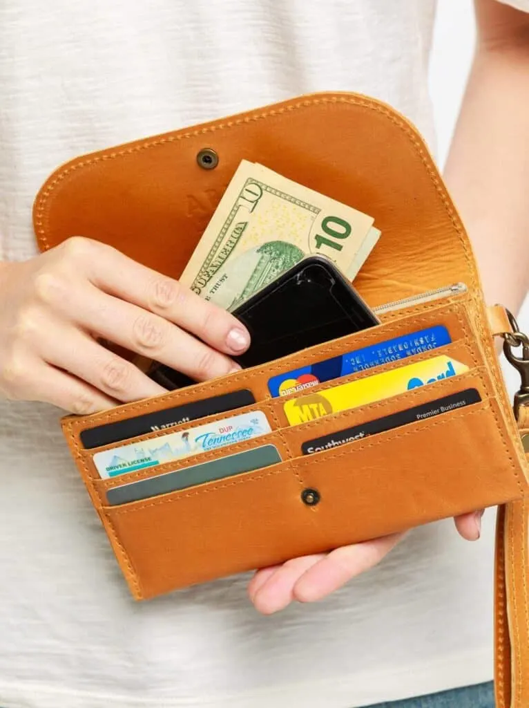 sustainable leather wallets, person holding open fold-over tan leather wallet showing off different cards and IDs while they put smartphone and money into the wallet