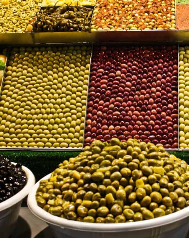 Explore the diverse foods of Spain, large market stall with hundreds of different coloured olives arranged for people to view and buy