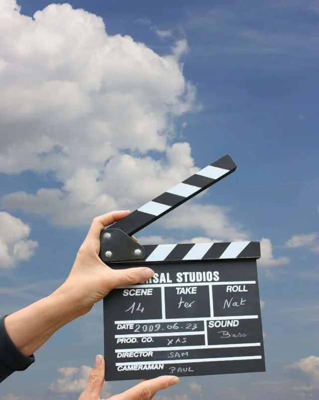 outdoor things to do in Milwaukee, hand holding a black and white Universal Studios movie clapper in the air with blue sky and clouds in background