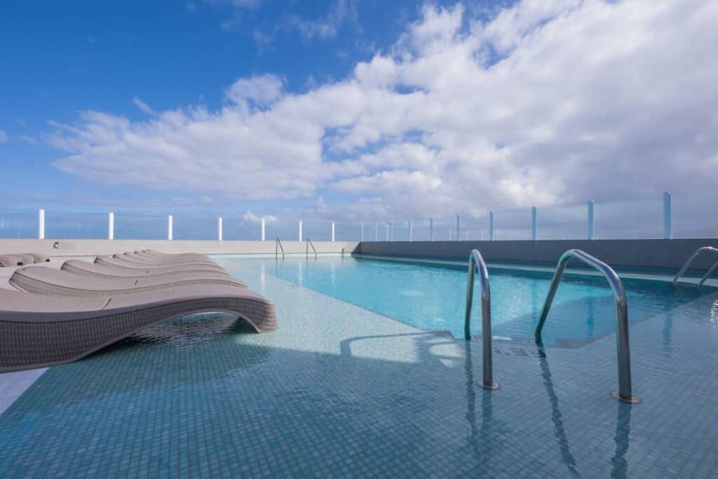 best mid-range Puerto de la Cruz accommodation, rooftop pool under a cloudy blue sky, pool is surrounded by blue tile and grey wicker pool beds