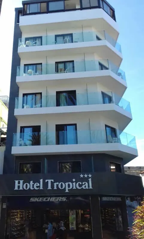 affordable Puerto de la Cruz hotels, exterior of 6-storey white building with glass balconies around each floor except top floor, first floor is painted black and the balcony reads Hotel Tropical *** and ground floor is a Sketchers shop