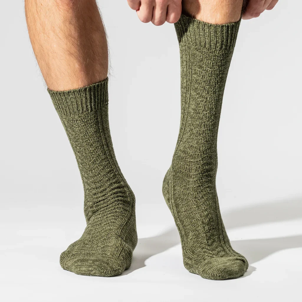 ethical wool socks, bttom of the legs of white personwearing knitted green socksand pulling up the right one