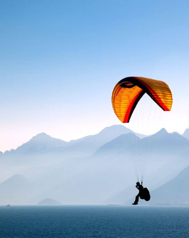 fun outdoor Tenerife south things to do, person paragliding near water with hazy mountains in the background under a clear blue sky at dusk