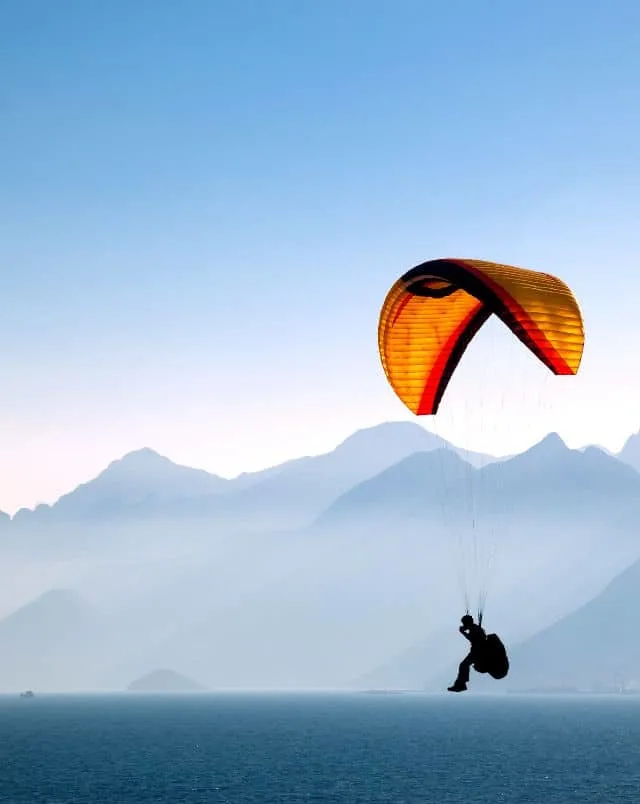 fun outdoor Tenerife south things to do, person paragliding near water with hazy mountains in the background under a clear blue sky at dusk