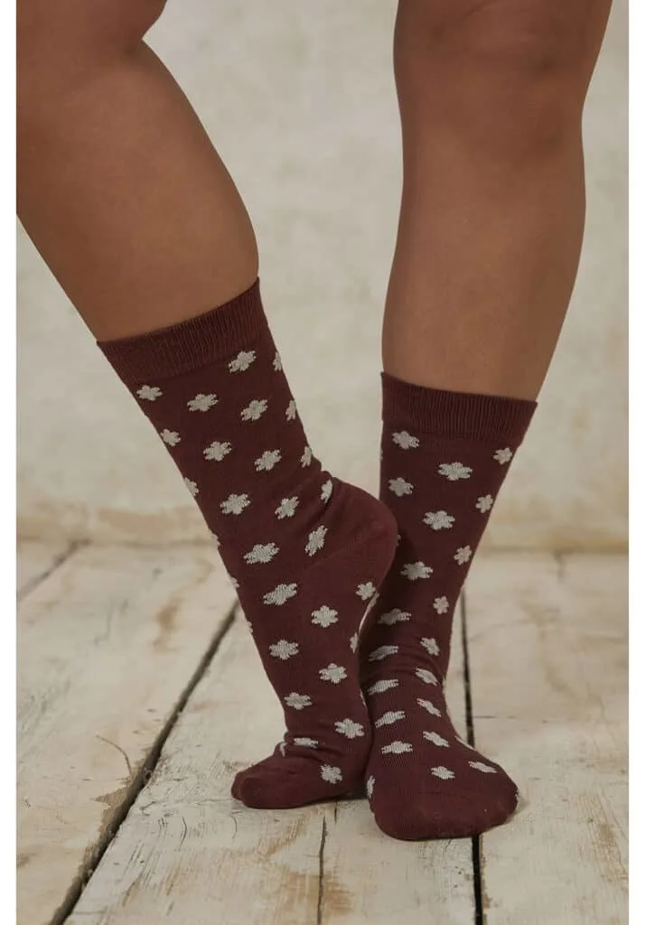 colorful ethical socks, legs of tan person wearing reddish brown mid-calf socks with white flowers