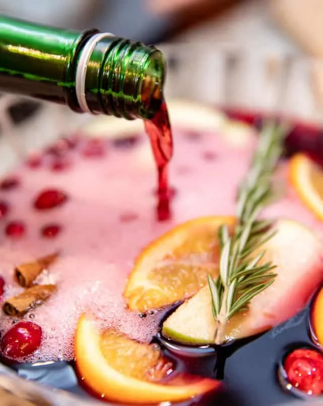 a wine bottle being poured in a fruit punch with orange slices