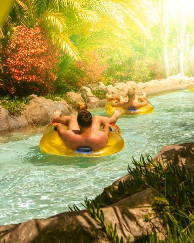 best things to do in south tenerife with kids, three people going down artificial river in yellow tubes surrounded by plants in siam park