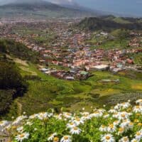 Amazing things to do in South Tenerife, view from a hilltop of valley with areas of houses and grassy fields surrounded by tall green hills with mountains in the distance