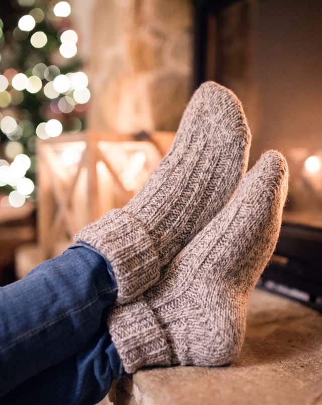 Amazing sustainable socks, feet in beige wool socks propped up on table with Christmas tree lights on in the background