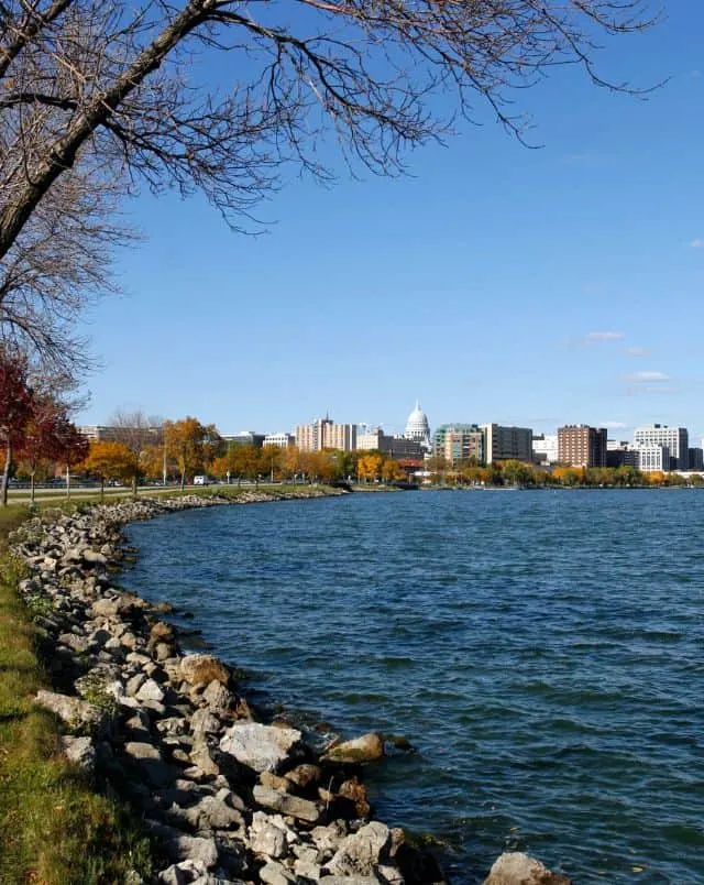 best Madison hiking trails, view of Madison Wisconsin skyline from curved lakeshore path lined with fall trees and rocks
