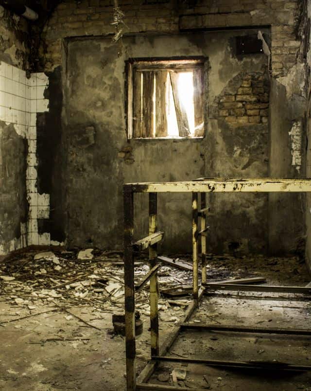 Journey to some of the abandoned places in America, interior of abandoned room with broken tiling on the walls and a broken boarded up window with light shining in on a burnt metal frame
