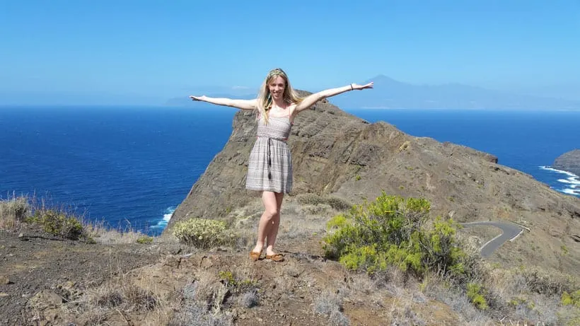 a woman on the rocks overlooking a beach and a hill