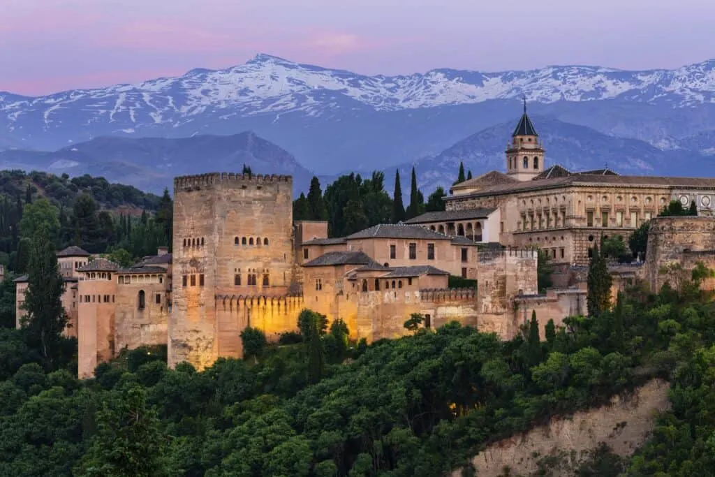 a view of Alhambra during sunset surrounded with trees and mountains at the back