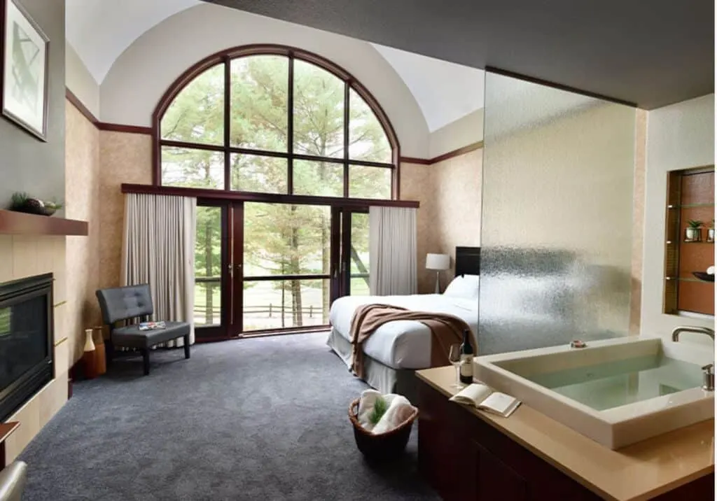 best romantic hotels in Wisconsin Dells high-ceilinged modern hotel room interior with large bed and huge bay windows next to frosted glass and bath/jacuzzi area