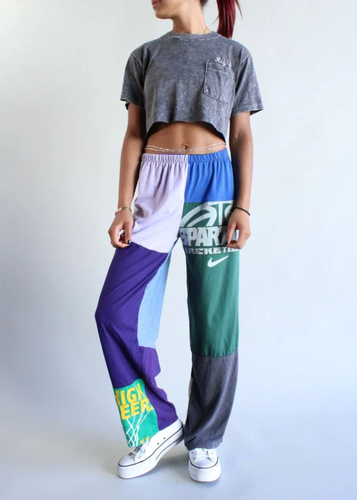 clothing brands made from recycled materials, image of white person from white down wearing grey crop top with pocket and loose fitting patchwork pants that have been made from other articles of clothing