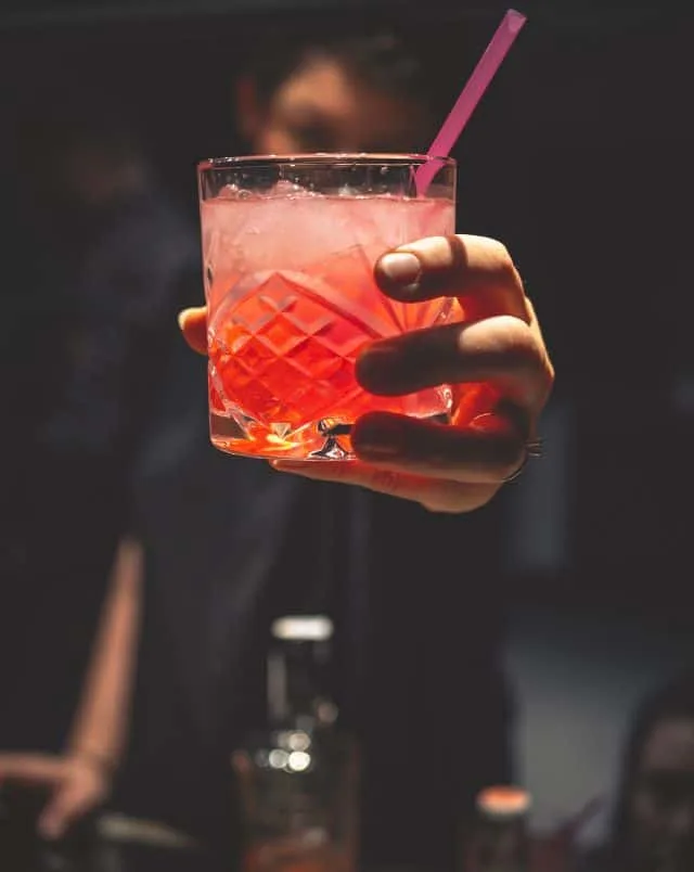 best things to do in October in Milwaukee for adults, close up of person holding out a red cocktail drink in a tumbler glass with a straw