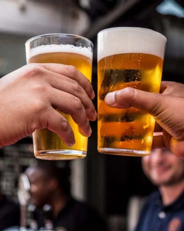 Taste the latest in famous Wisconsin beer, close up shot of two beers being clinked together by two hands with people in the background