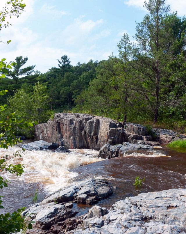 Enjoy these fun things to do in Eau Claire, waterfall cascading down rocky terrain with green trees behind