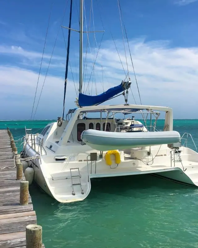 Find out about what is there to do in cape verde, back view of a catamaran docked next to wooden pier in green-blue water under a cloudy blue sky