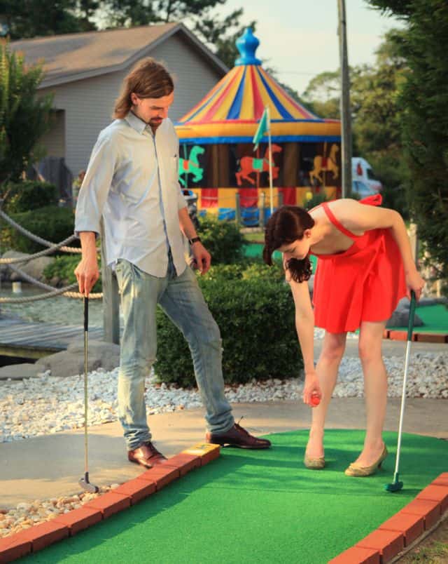 two people standing on a mini golf course with children's carousel behind at one of the best golf resorts in wisconsin